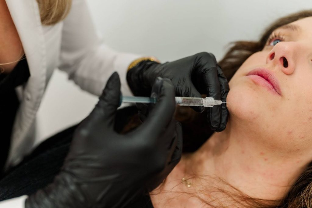 A specialist is injecting filler into a customer’s chin to enhance her facial appearance.